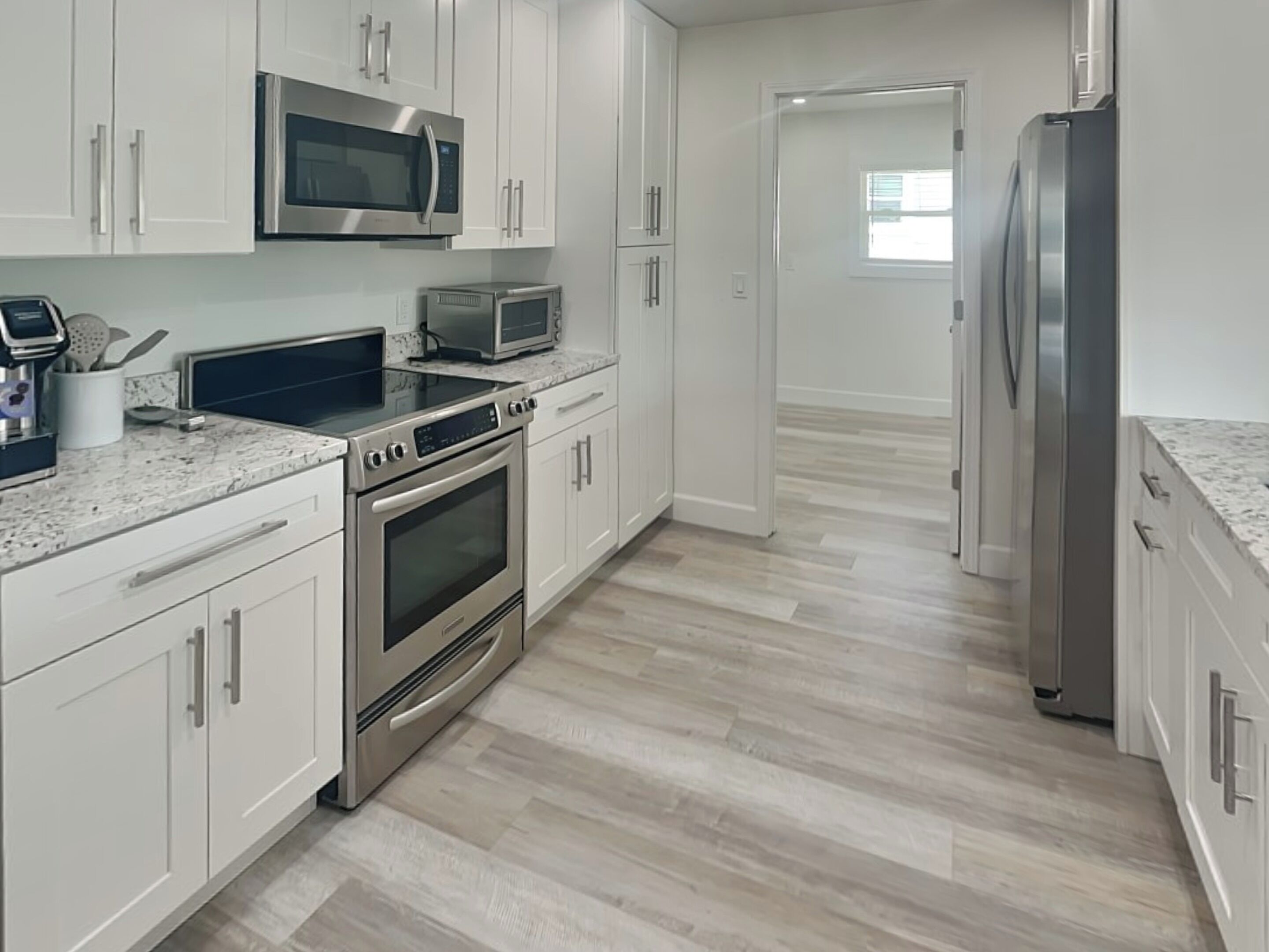 A modern kitchen with white cabinets, stainless steel appliances, and a marble countertop.