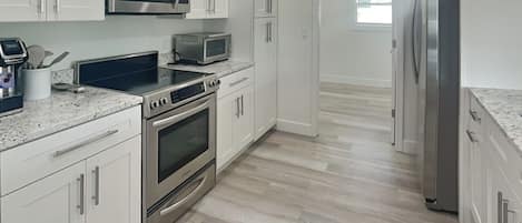 A modern kitchen with white cabinets, stainless steel appliances, and a marble countertop.