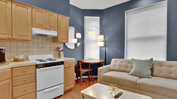 A compact kitchen with a stove, oven, and wooden cabinets, a dining area with a table and chairs, and a sofa with a cushion. - Historic Rittenhouse 2BR Loft | Sleeps 12 | Philly (Philadelphia)
