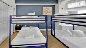 Una habitación con literas, un escritorio con lámpara, un cuadro en la pared y un ventanal con vidrieras decorativas.