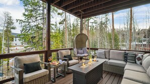 A covered outdoor seating area with wicker furniture, a hanging chair, and a fire feature.