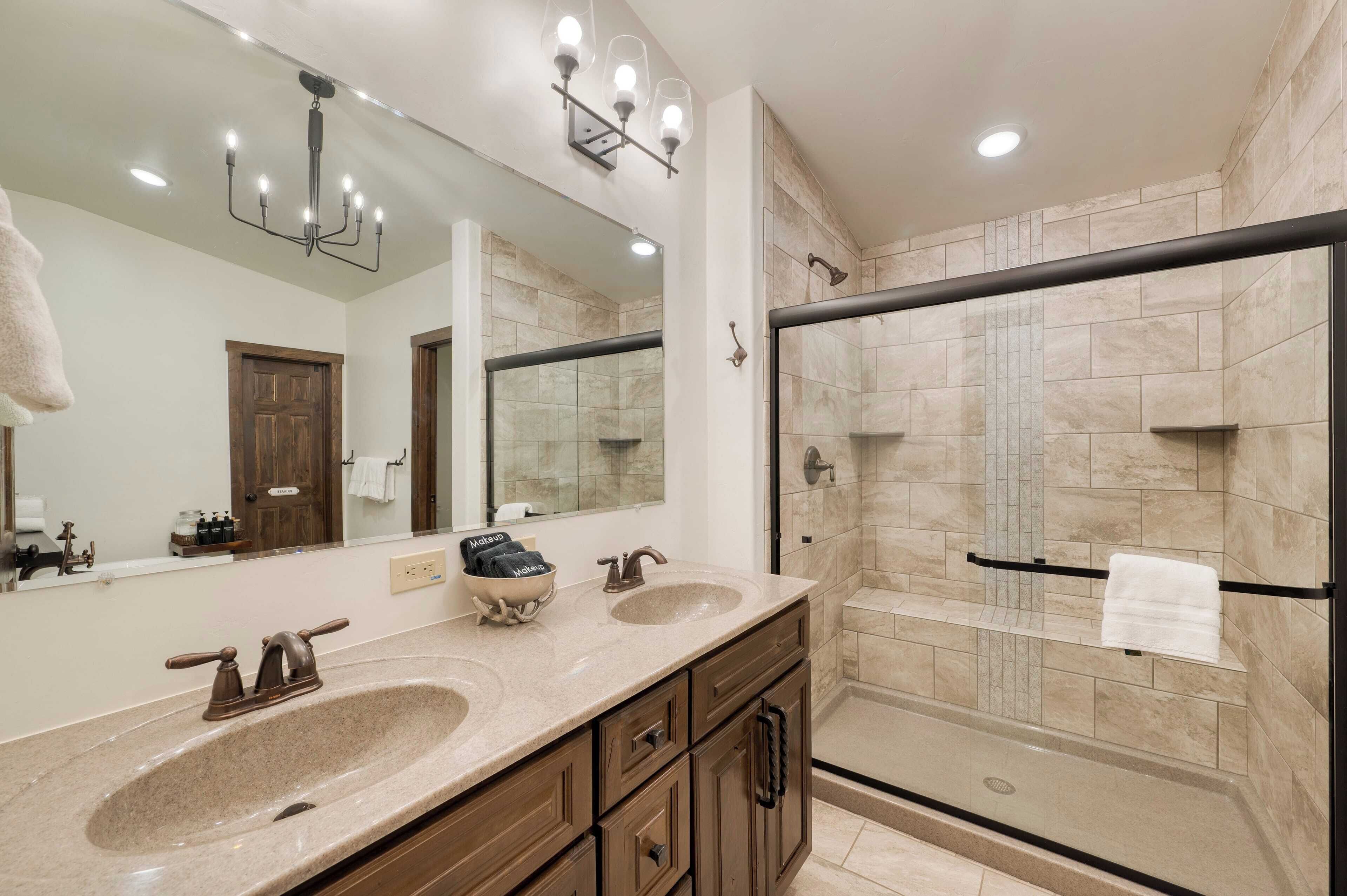 A bathroom with two sinks, a large mirror, and a glass-enclosed shower.