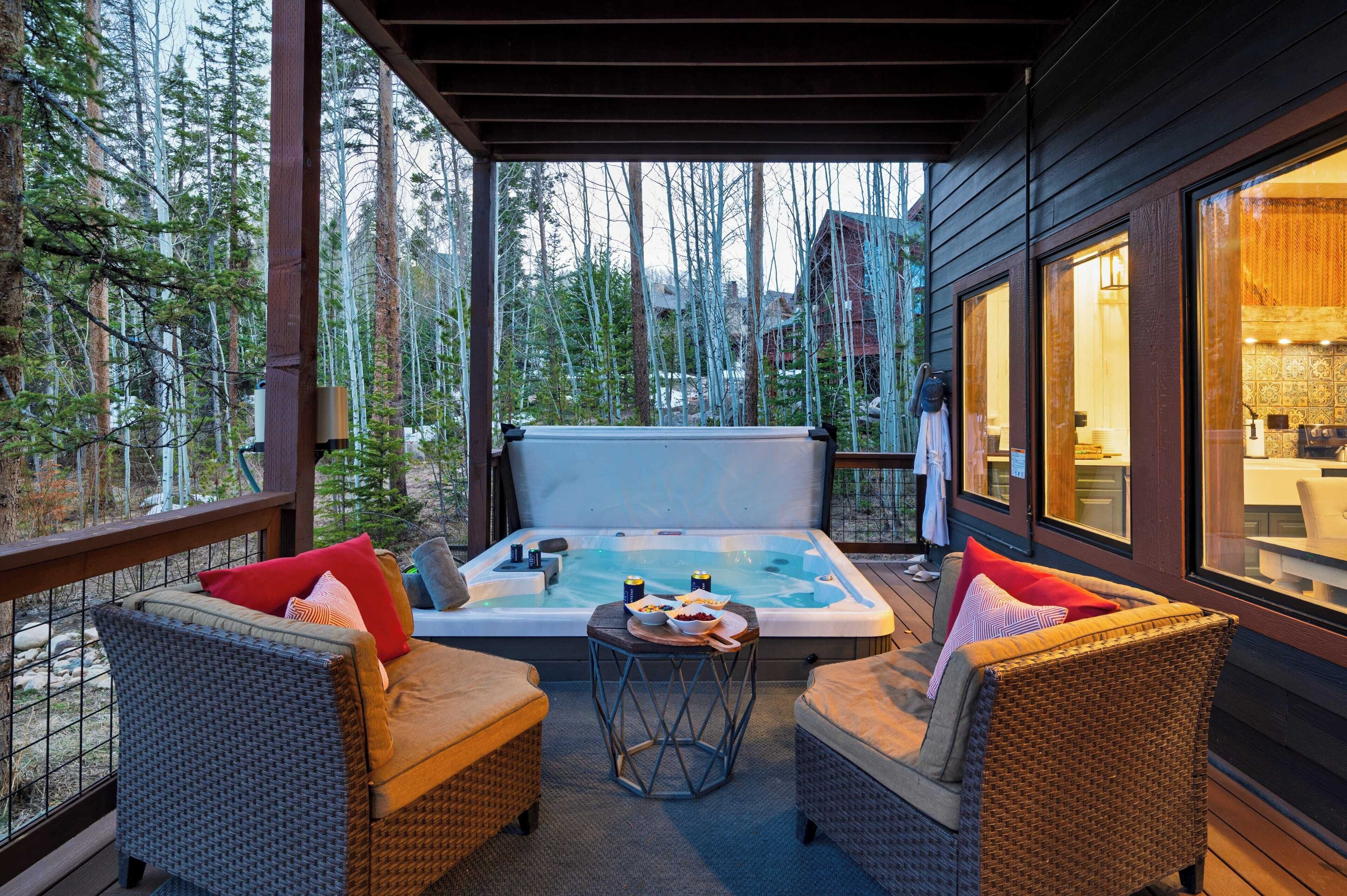 A wooden deck with wicker furniture and a hot tub, surrounded by tall trees.