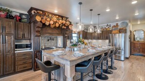 A spacious kitchen with a large island, wooden cabinets, and a variety of cookware displayed on the wall.