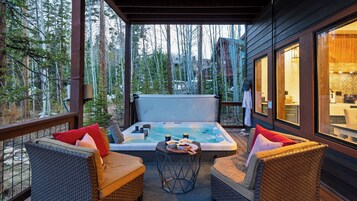 Terraza de madera con jacuzzi, sillas de mimbre y una mesa de comedor con un tazón y bebidas.