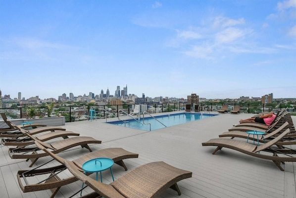 A rooftop pool with lounge chairs, a city skyline view, and a clear sky.