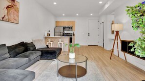 A modern living room with a grey sofa, a glass coffee table, and a potted plant.