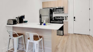 A compact kitchen with a refrigerator, microwave, and stove. There are two bar stools and a small sink area.