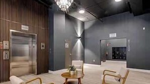 A modern lobby with a wooden reception desk, a chandelier, and a seating area with two chairs and a small round table.