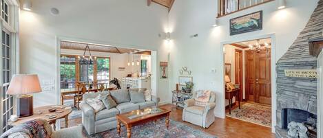 A spacious living room with a high ceiling, a stone fireplace, and a view of the outdoors.
