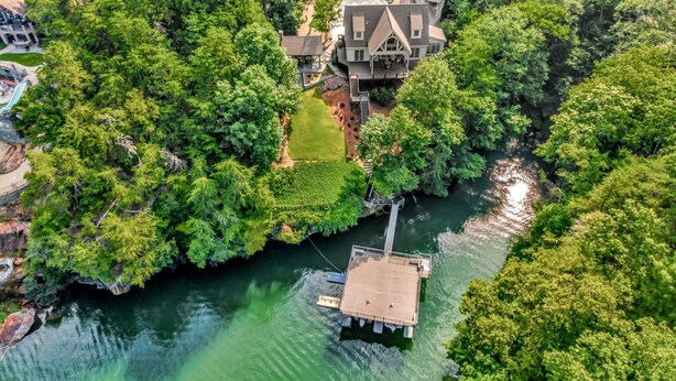Una casa grande rodeada de un bosque frondoso, un muelle y un bote pequeño.