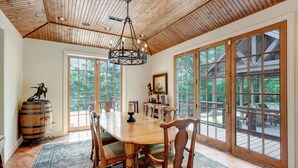 Comedor con mesa de madera, sillas y una lámpara de araña. Amplias ventanas y vistas al exterior.