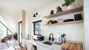 Una cocina moderna con estantes de madera, una cafetera y una ventana con vistas a la vegetación.