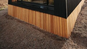 Una cabaña moderna con techo triangular, amplias ventanas y revestimiento de madera.