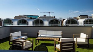 A rooftop patio with outdoor seating, a pergola, and a view of modern buildings and a construction crane in the background. - Cultural District Loft, Rooftop Terrace + Games (Fort Worth)