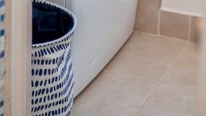 A compact, modern laundry room with a front-loading washing machine, a small trash bin, and a tiled floor.