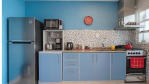 A kitchen with a blue refrigerator, a microwave, a coffee maker, a kettle, and a stove.