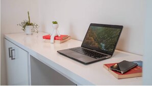 A laptop on a desk with a plant, books, and a smartphone.