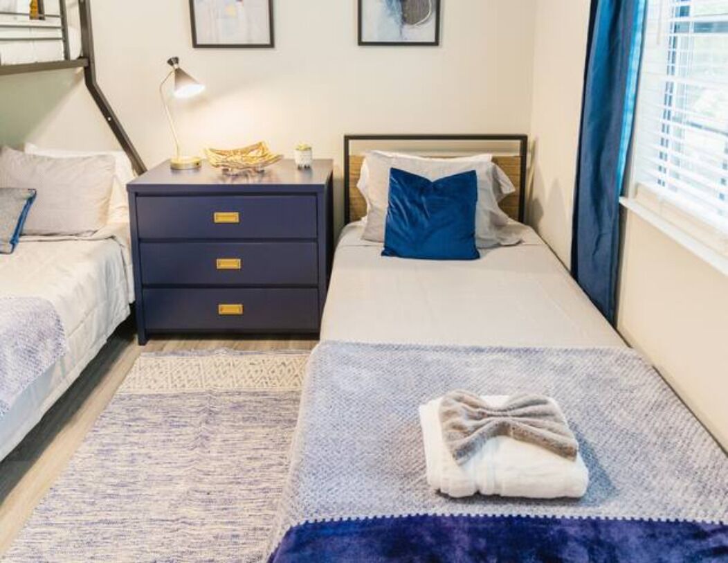Un dormitorio con cama, mesita de noche, cómoda y ventana con cortinas.