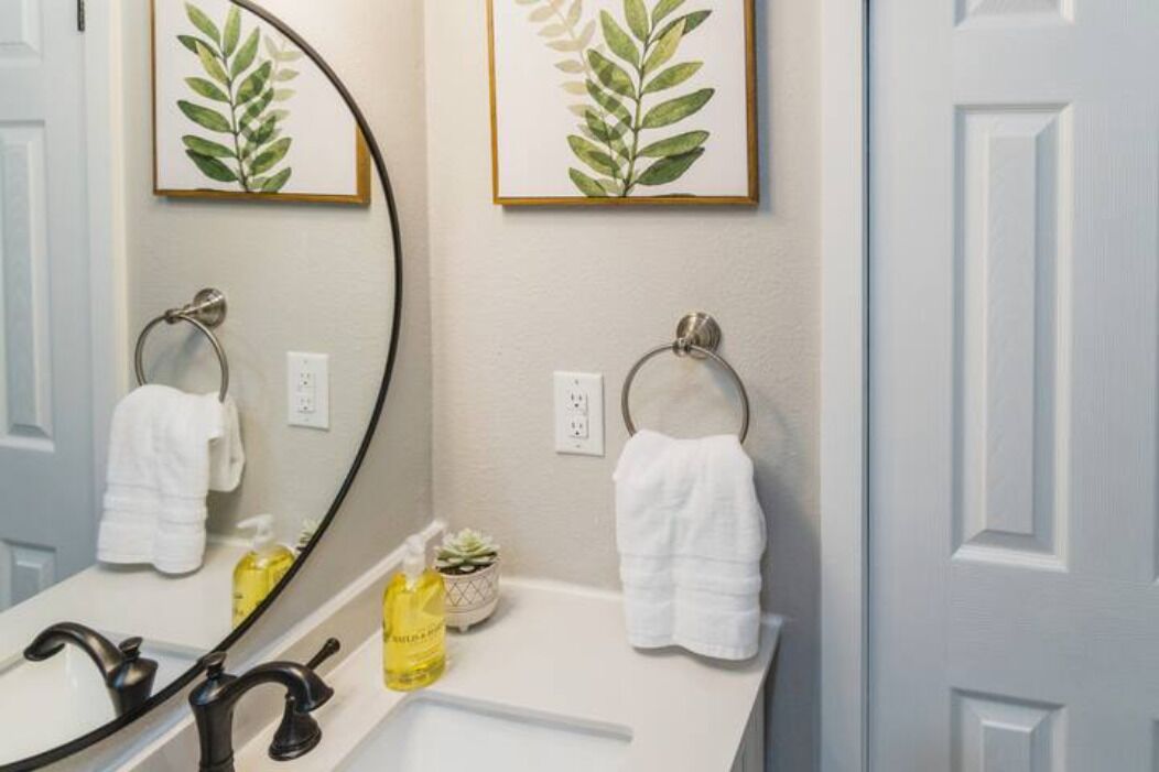 Une salle de bain avec un grand miroir, deux porte-serviettes, un lavabo et deux œuvres d’art représentant des feuilles, encadrées et accrochées au mur.