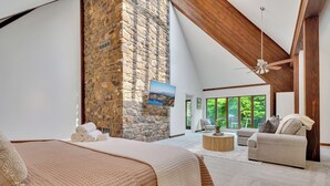 Ein Schlafzimmer mit Steinwand, einem großen Bett, einem Deckenventilator und Blick ins Freie.
