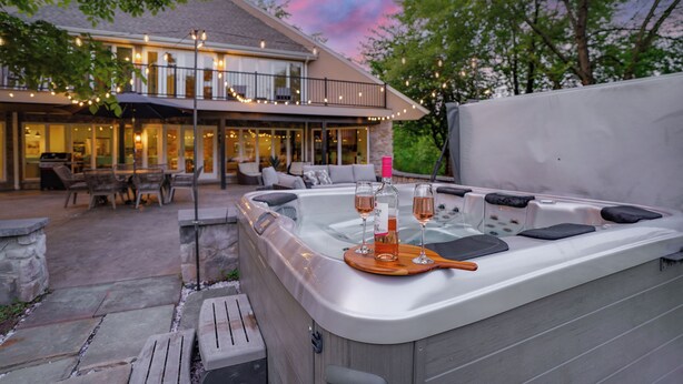 Ein Whirlpool mit zwei Weingläsern und einer Flasche, umgeben von Steinbänken und einer Holzterrasse.