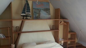 A bedroom with a bed, wooden shelves, a hanging light fixture, and a painting on the wall.