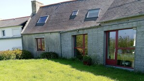 A two-story stone house with a sloped roof, a red door, and a small window.