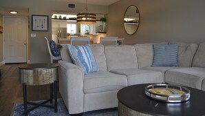 Ein Wohnzimmer mit einer Eckcouch, einem Couchtisch, einem Beistelltisch und einer Küche im Hintergrund.