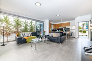 A modern living room with a sofa, coffee table, and a view of the kitchen. - Blue Pelagos Villa in Protaras (Paralimni)
