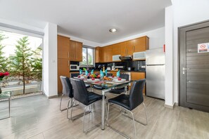 A modern kitchen with wooden cabinets, stainless steel appliances, and a glass dining table with black chairs. - Blue Pelagos Villa in Protaras (Paralimni)