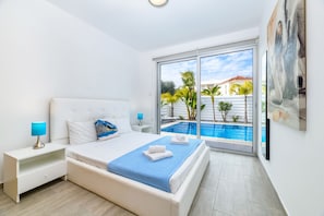 Een moderne slaapkamer met een groot bed, een nachtkastje, een lamp en uitzicht op een zwembad door een glazen deur.
