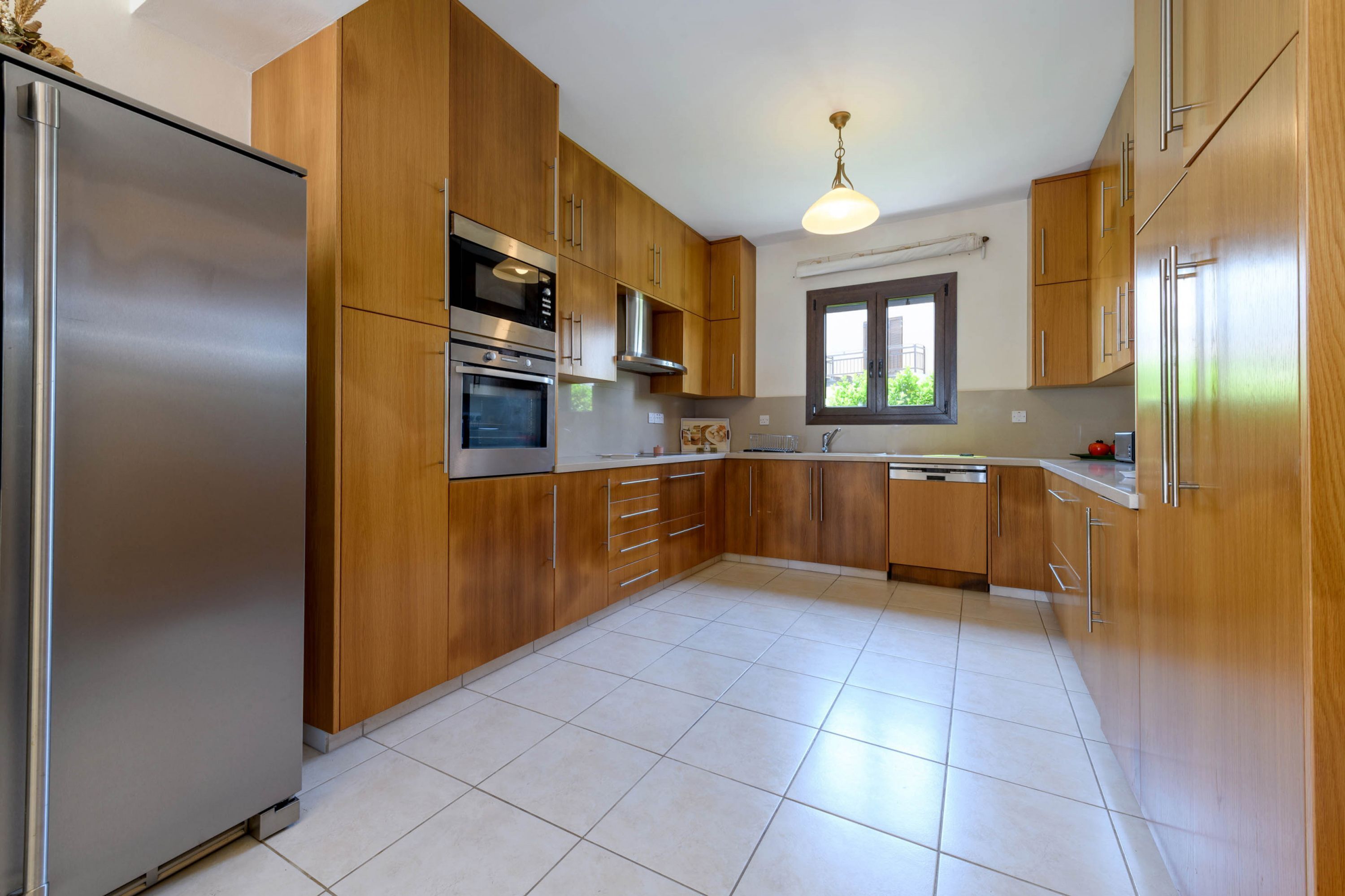 A modern kitchen with wooden cabinets, stainless steel appliances, and a tiled floor.