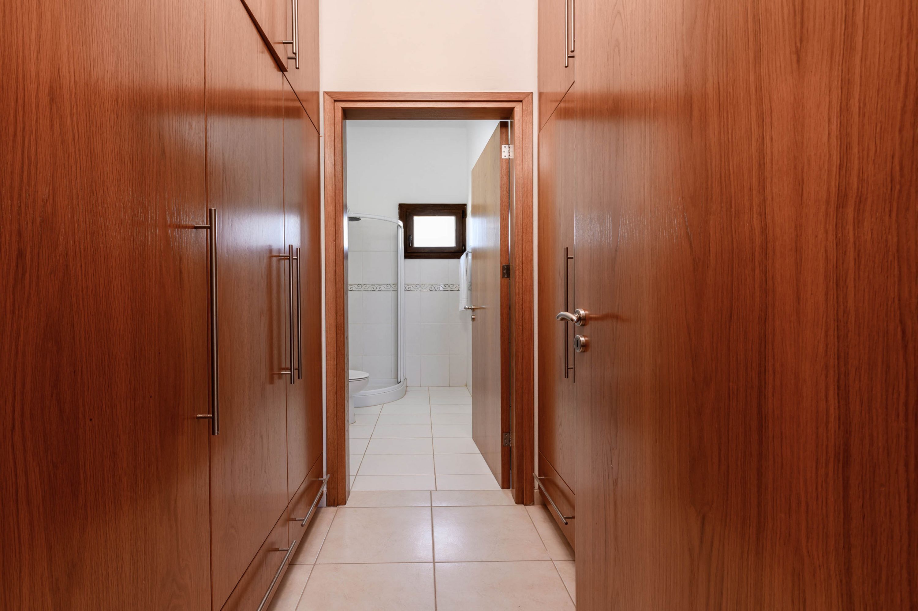 Un couloir avec des portes en bois menant à une salle de bain équipée de toilettes et d’une fenêtre.