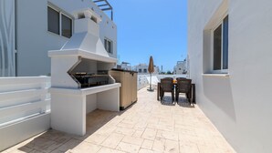 Eine Dachterrasse mit Grill, Sitzgelegenheiten im Freien und Blick auf andere Gebäude.