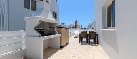 Una terraza en la azotea con una parrilla, mobiliario exterior y vistas a otros edificios.