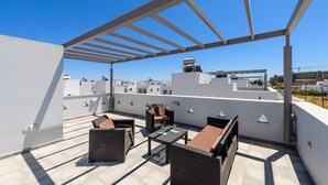 Eine Dachterrasse mit Gartenmöbeln, einer Pergola und Blick auf die Stadt.