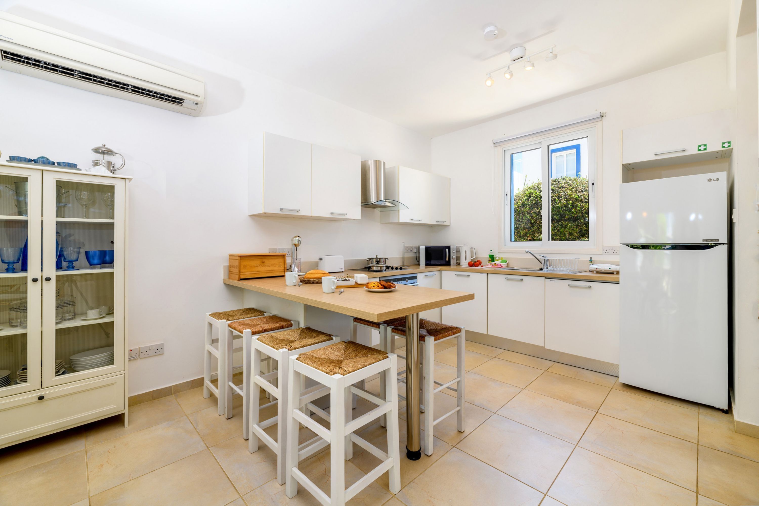A modern kitchen with white cabinets, a central island with stools, a built-in microwave, and a refrigerator.