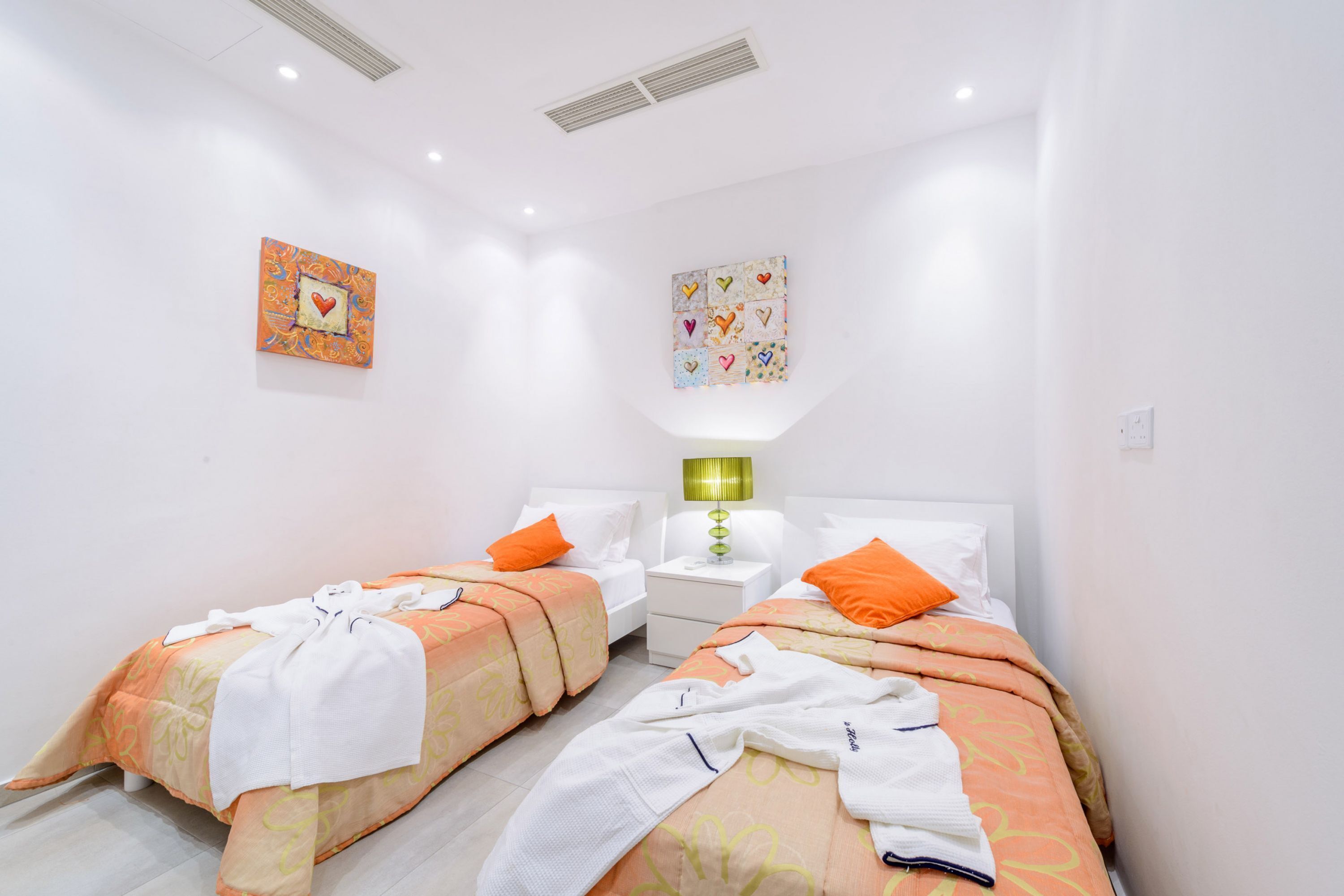 Habitación de hotel con dos camas, paredes blancas e iluminación empotrada en el techo.