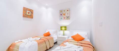 Habitación de hotel con dos camas, paredes blancas e iluminación empotrada en el techo.