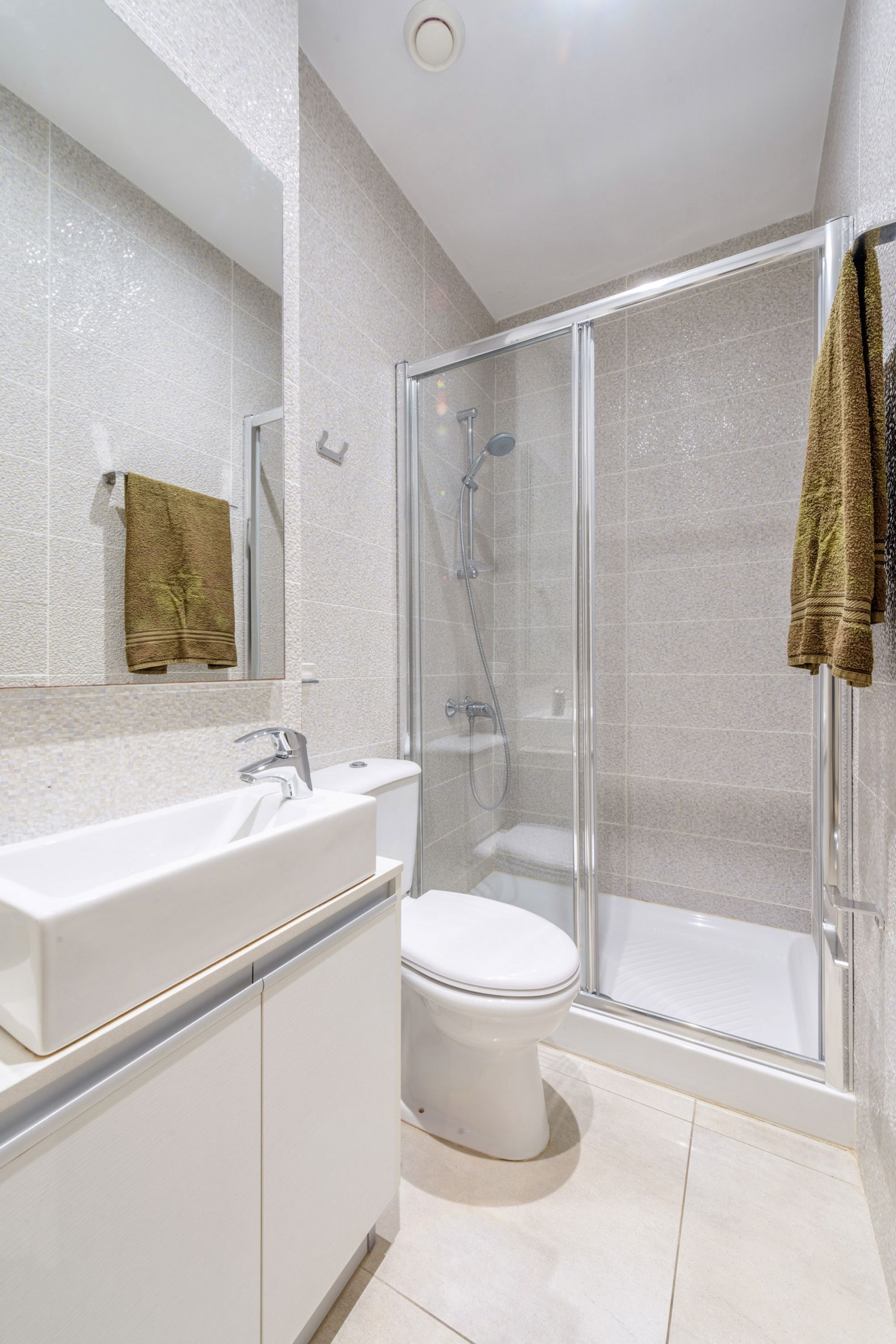 Een moderne badkamer met een douchecabine van glas, een witte wastafel en een toilet.
