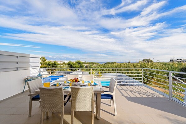 A terrace with a pool, wicker furniture, and a table set with fruits and drinks.