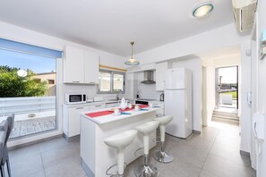 Una cocina moderna con armarios blancos, una isla central con taburetes y electrodomésticos como microondas y refrigerador.