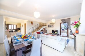 A modern living room with a white sofa, a dining area with a set table, and a staircase leading to an upper floor.