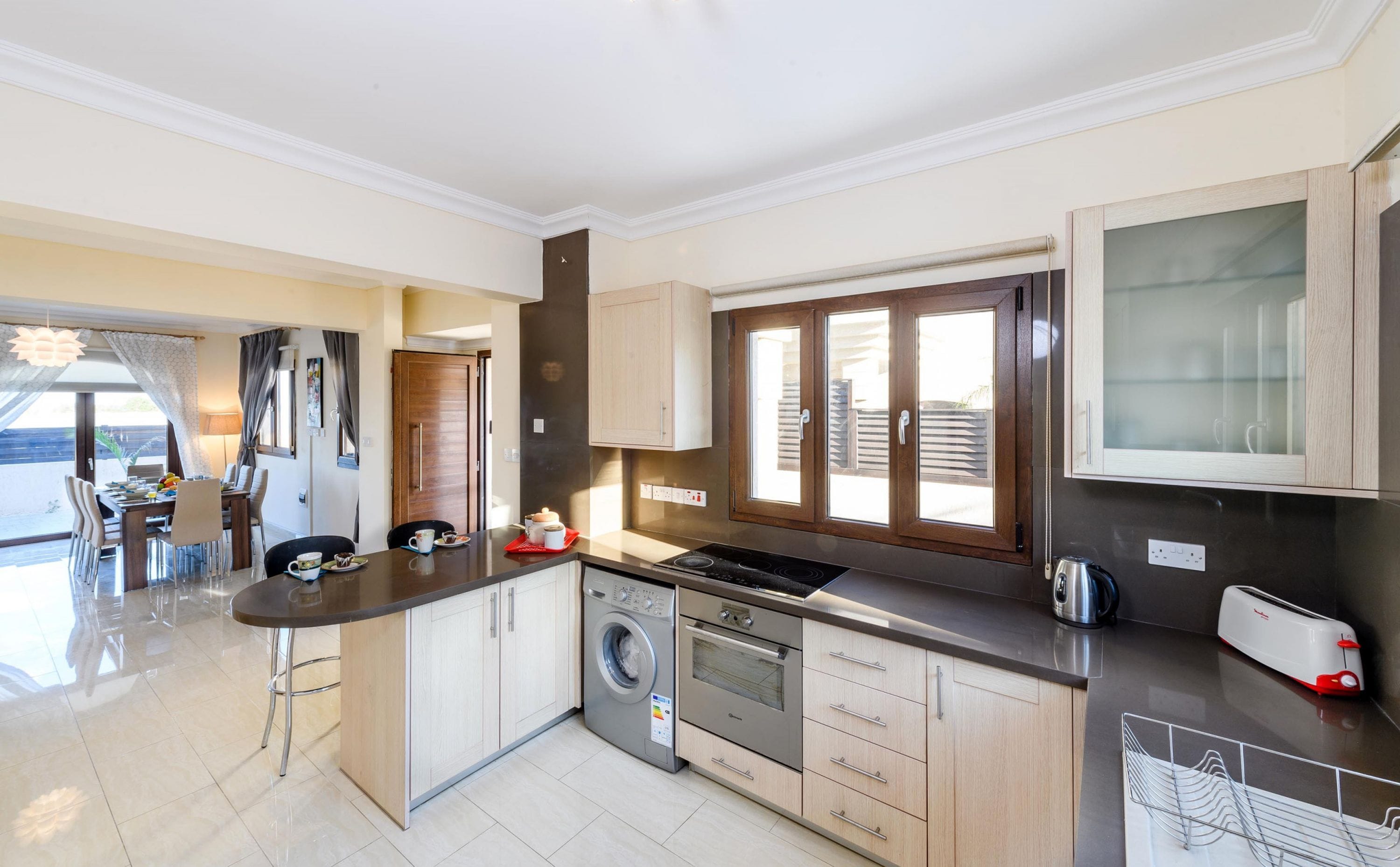 A modern kitchen with a central island, built-in appliances, and a dining area with a view.