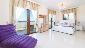 Une chambre moderne avec un grand lit, un fauteuil violet et une vue sur la mer grâce à de grandes fenêtres du sol au plafond.