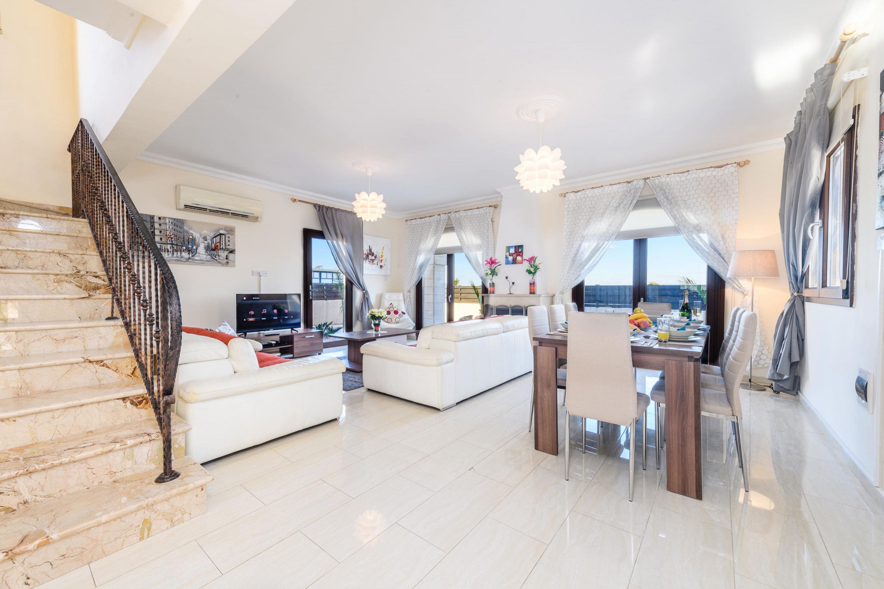 A spacious living area with a white sofa, dining table, and a staircase with a metal railing.