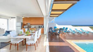 Un intérieur moderne comprenant un coin repas, une cuisine et un salon avec accès à la piscine, équipé de chaises longues.