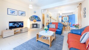 A modern living room with a TV, sofa, and coffee table. There is a dining area with a table and chairs. - Villa Penelope in Protaras (Paralimni)