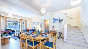 A spacious living area with a dining table set for six, surrounded by wooden chairs with blue cushions. A staircase is visible to the right, leading to an upper floor. - Villa Penelope in Protaras (Paralimni)